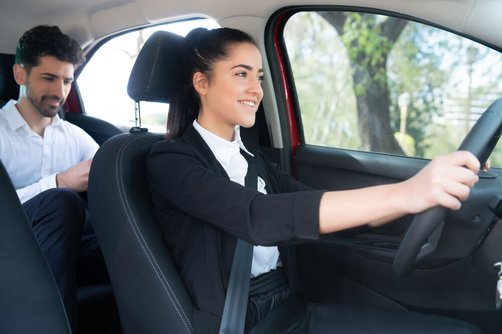 Female cab driver smiling while driving, showing BAWA GUEST HOUSE trusted by 4880 customers 